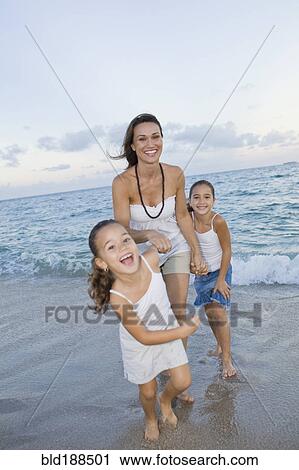 Stock Image - Multi-ethnic mother and daughters playing in surf. Fotosearch