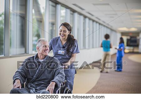 Stock Image - Nurse pushing patient in wheelchair. Fotosearch