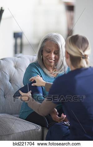 Nurse taking patient blood pressure in living room View Large Photo Image Picture - Nurse taking patient blood pressure in living room. Fotosearch