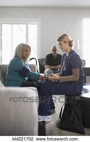 Stock Image - Nurse taking patient blood pressure in living room. Fotosearch