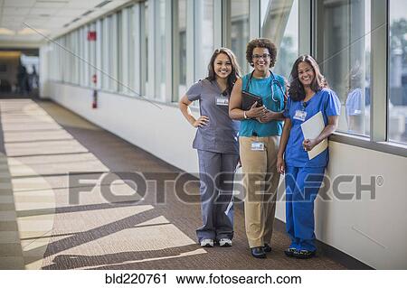 Stock Image - Nurses and doctor smiling in hospital hallway. Fotosearch