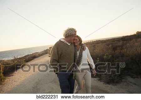Stock Image - Older Caucasian couple walking on dirt path. Fotosearch