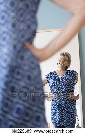 Stock Photo - Older Caucasian woman admiring dress in mirror . Fotosearch