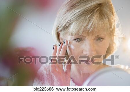 Stock Photograph - Older Caucasian woman applying moisturizer to face. Fotosearch