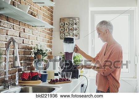 Stock Photograph - Older Caucasian woman blending smoothie in kitchen. Fotosearch
