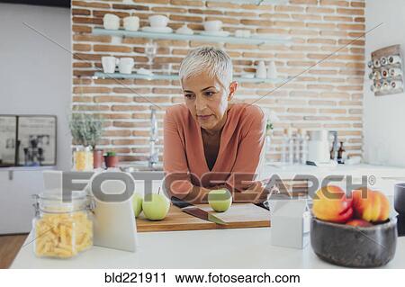 Stock Image - Older Caucasian woman cooking in kitchen. Fotosearch