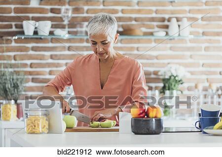 Stock Image - Older Caucasian woman cutting apples in kitchen. Fotosearch