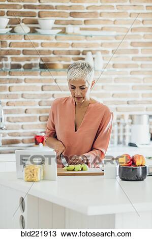 Stock Image - Older Caucasian woman cutting apples in kitchen. Fotosearch