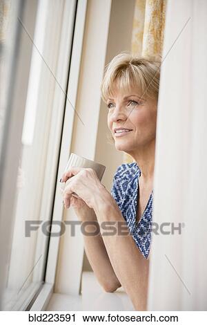 Stock Image - Older Caucasian woman drinking coffee at window. Fotosearch