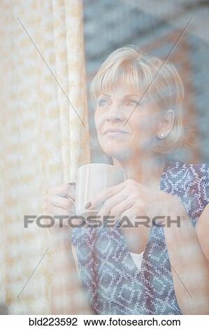 Stock Image - Older Caucasian woman drinking coffee at window. Fotosearch