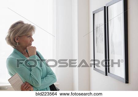 Picture - Older Caucasian woman examining artwork in gallery. Fotosearch
