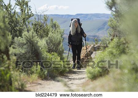 Stock Photo - Older Caucasian woman hiking with backpack on path. Fotosearch