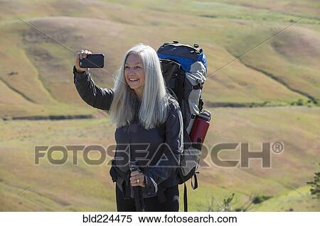 Stock Photography - Older Caucasian woman hiking with backpack taking selfie. Fotosearch
