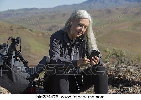 Stock Photograph - Older Caucasian woman listening to cell phone on mountain. Fotosearch