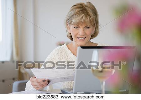 Stock Image - Older Caucasian woman paying bills using laptop. Fotosearch