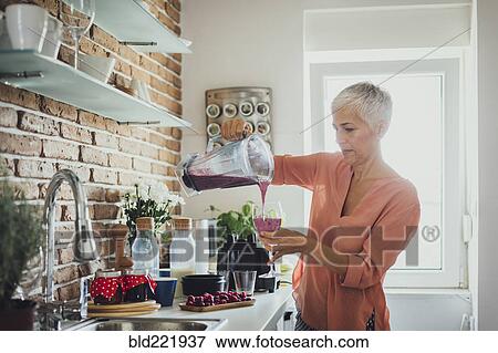 Stock Photo - Older Caucasian woman pouring smoothie in kitchen. Fotosearch