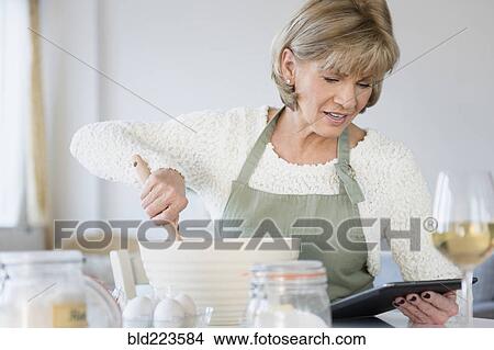 Picture - Older Caucasian woman reading recipe on digital tablet. Fotosearch