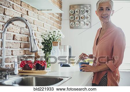 Stock Image - Older Caucasian woman stirring coffee in kitchen. Fotosearch