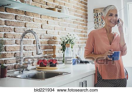 Older Caucasian woman talking on cell phone in kitchen View Large Photo Image Picture - Older Caucasian woman talking on cell phone in kitchen. Fotosearch