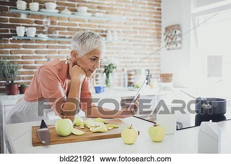 Older Caucasian woman using digital tablet in kitchen View Large Photo Image Stock Image - Older Caucasian woman using digital tablet in kitchen. Fotosearch