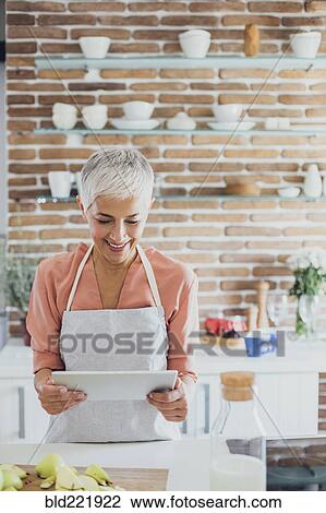 Older Caucasian woman using digital tablet in kitchen View Large Photo Image Stock Image - Older Caucasian woman using digital tablet in kitchen. Fotosearch