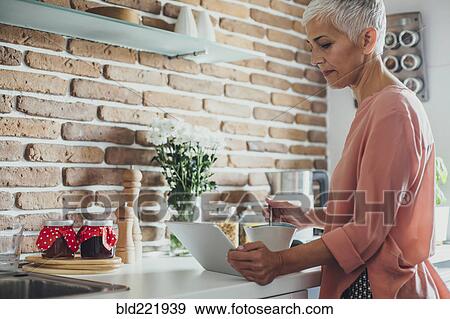 Stock Photo - Older Caucasian woman using digital tablet in kitchen. Fotosearch