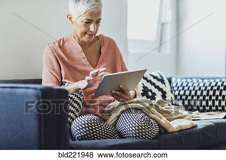 Older Caucasian woman using digital tablet on sofa View Large Photo Image Stock Photo - Older Caucasian woman using digital tablet on sofa. Fotosearch