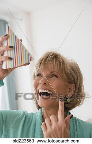 Stock Image - Older Caucasian woman wearing party hat. Fotosearch