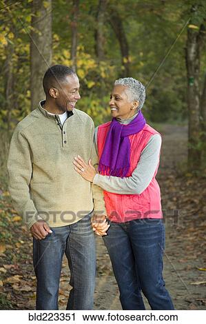 Stock Image - Older couple holding hands walking in forest. Fotosearch