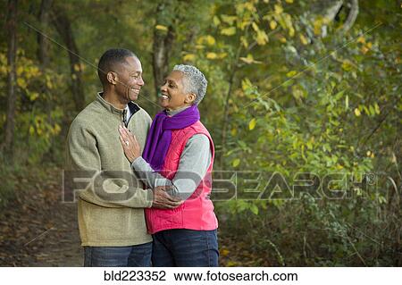 Stock Image - Older couple holding hands walking in forest. Fotosearch