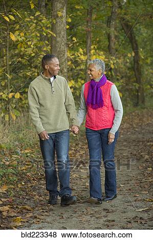 Stock Photo - Older couple holding hands walking in forest. Fotosearch