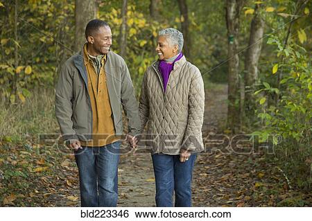 Stock Photograph - Older couple holding hands walking in forest. Fotosearch