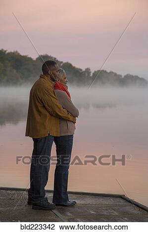 Stock Image - Older couple hugging at foggy river at sunrise. Fotosearch