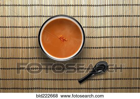 Stock Photo - Orange soup in bowl with black spoon. Fotosearch