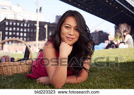Stock Image - Pacific Islander woman laying on grass with picnic basket. Fotosearch