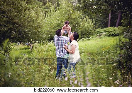 Stock Image - Parents holding baby in garden. Fotosearch