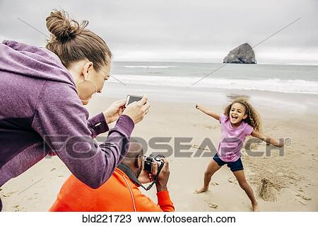 Stock Image - Parents photographing daughter on beach. Fotosearch