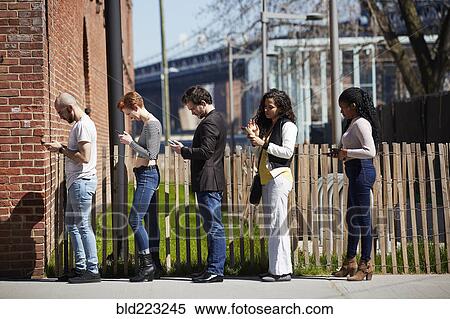 Stock Photography - People in line on sidewalk using cell phones. Fotosearch