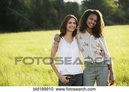 Stock Image - Portrait of two women hugging in meadow. Fotosearch