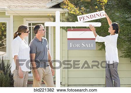 Stock Image - Real estate agent hanging sign outside house. Fotosearch