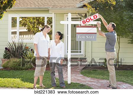 Stock Image - Real estate agent hanging sign outside house. Fotosearch
