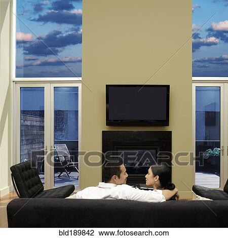 Stock Image - Rear view of Asian couple on sofa. Fotosearch