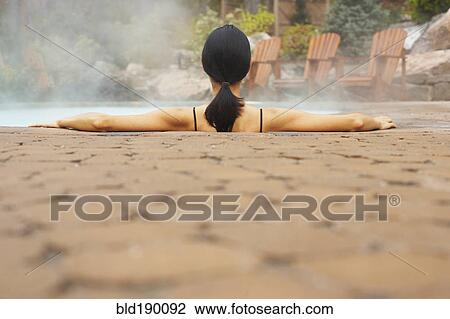 Stock Image - Rear view of woman sitting in hot tub. Fotosearch