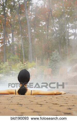 Stock Image - Rear view of woman sitting in hot tub. Fotosearch