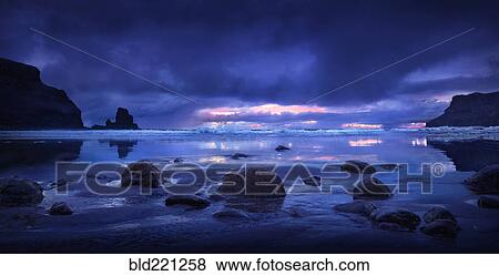 Stock Photo - Rocks on beach under storm clouds. Fotosearch