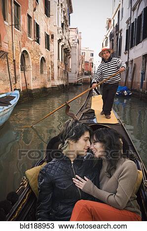 Stock Image - Romantic Italian couple riding in gondola through canal. Fotosearch