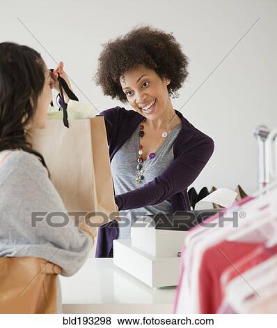 Sales clerk handing customer shopping bag View Large Photo Image Stock Photo - Sales clerk handing customer shopping bag. Fotosearch