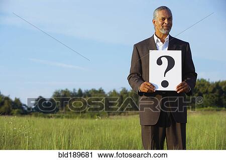 Stock Image - Senior African businessman holding question mark in field. Fotosearch