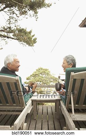 Stock Image - Senior Asian couple drinking coffee and talking outdoors. Fotosearch