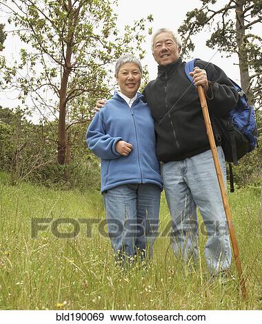 Stock Photo - Senior Asian couple with backpack and walking stick outdoors. Fotosearch